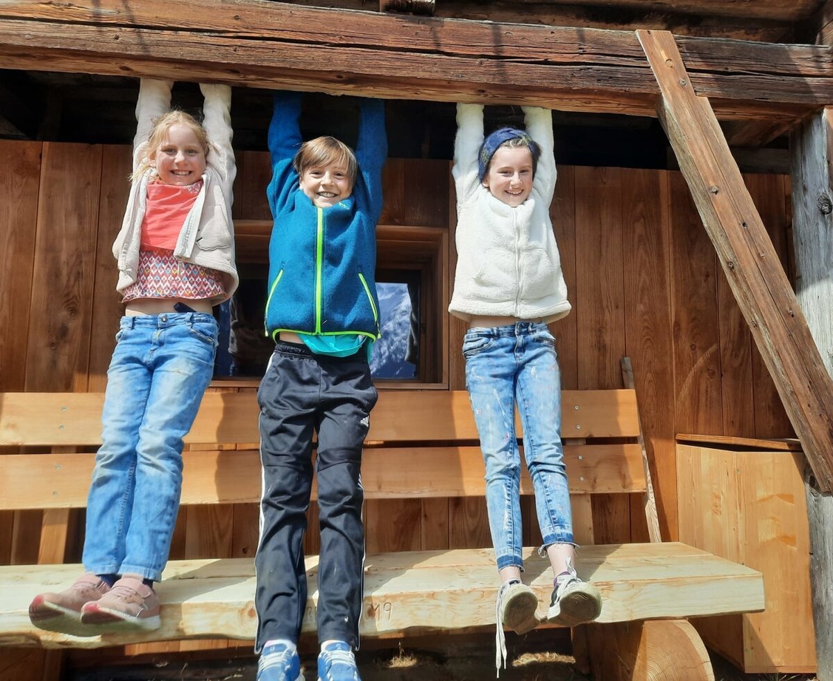 Bambini che giocano su una trave di legno nell'agriturismo, con una panca di legno nell'area esterna.