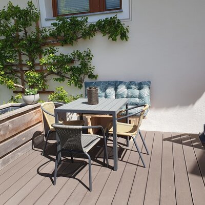 Terrazza dell'agriturismo con tavolo da pranzo, quattro sedie e una panca imbottita, circondata da piante.