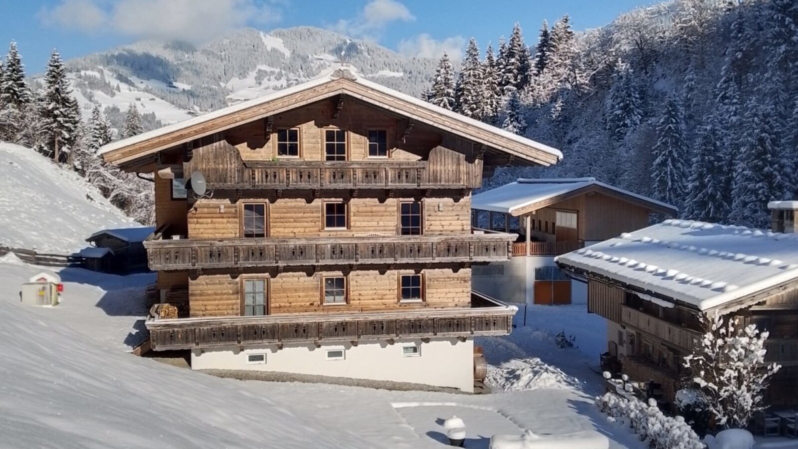 La fattoria in un ambiente invernale, con facciata in legno, balconi e montagne innevate sullo sfondo.