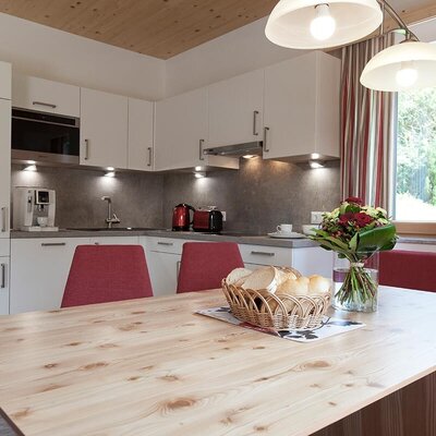 Una moderna cucina abitabile nell'appartamento, con un tavolo da pranzo in legno chiaro, un'accogliente area salotto e un angolo cottura completamente attrezzato.