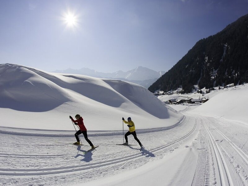 Due sciatori di fondo su una pista nel paesaggio invernale soleggiato con vista sulle montagne.