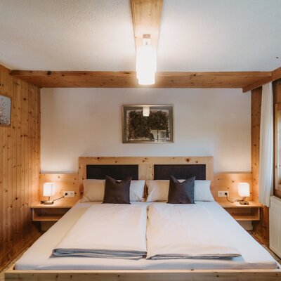 Camera matrimoniale in agriturismo con rivestimento in legno, letto matrimoniale, comodini e finestra.