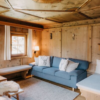 Soggiorno rivestito in legno con divano, tavolo di legno, panche e finestra.