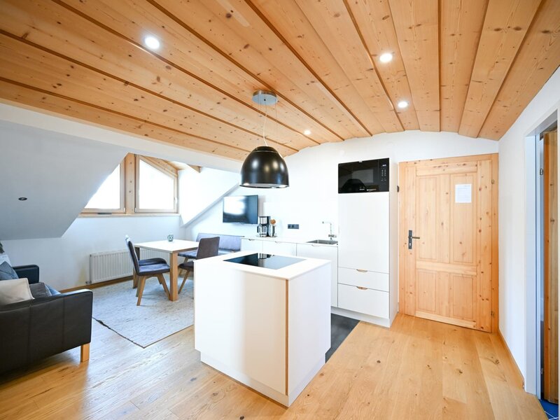 Zona giorno a pianta aperta dell'appartamento nell'agriturismo, con cucina moderna a isola, zona pranzo, divano e soffitto in legno.