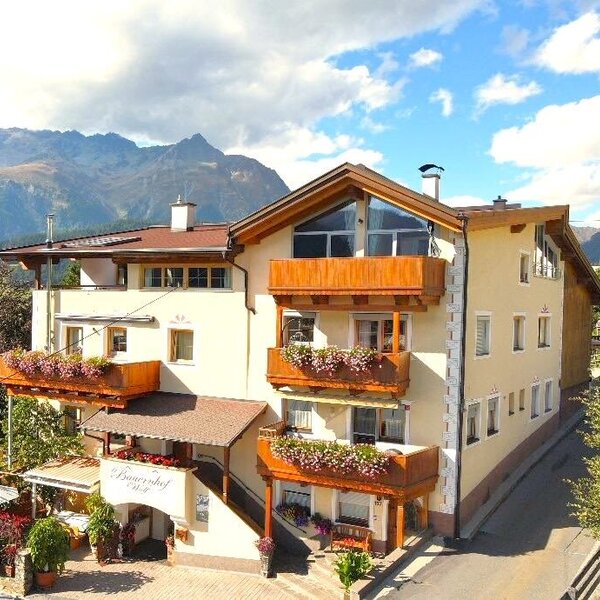 Vista esterna del maso con balconi fioriti, una terrazza solarium e vista sulle montagne.