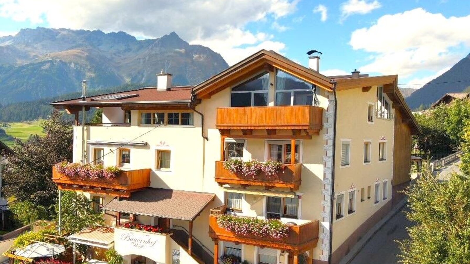 Vista esterna del maso con balconi fioriti, una terrazza solarium e vista sulle montagne.