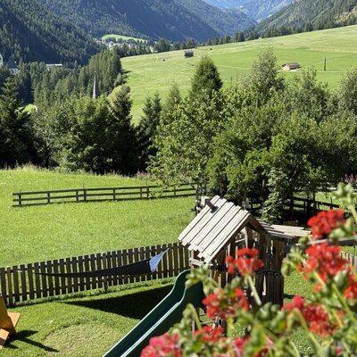 Parco giochi per bambini con scivolo e sedie a sdraio sul prato del maso, con vista sui campi verdi circostanti e sulle montagne.