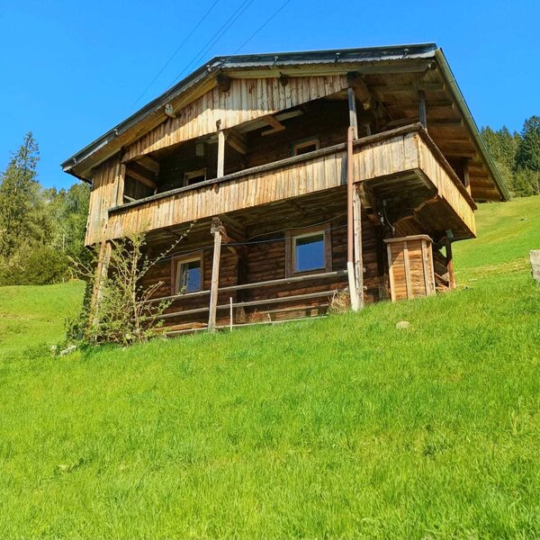 L'esterno dell'Alm, un edificio in legno a due piani con balcone su un pendio erboso.