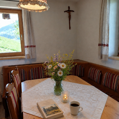 Un'accogliente zona pranzo nell'Alm con una tipica panca ad angolo in legno, fiori di campo e un tavolo apparecchiato con cura.