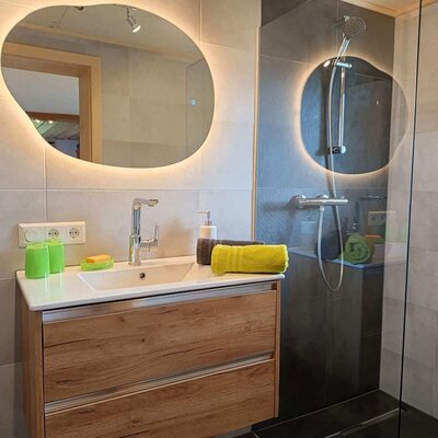 Bagno moderno nell'agriturismo con lavabo, specchio illuminato e doccia a filo pavimento.