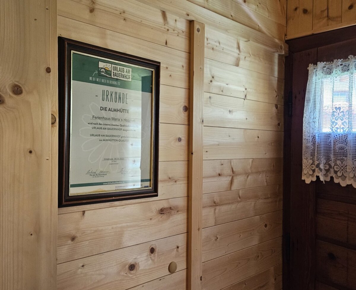 La rustica parete in legno del con un certificato incorniciato accanto a una tenda ricamata in pizzo.