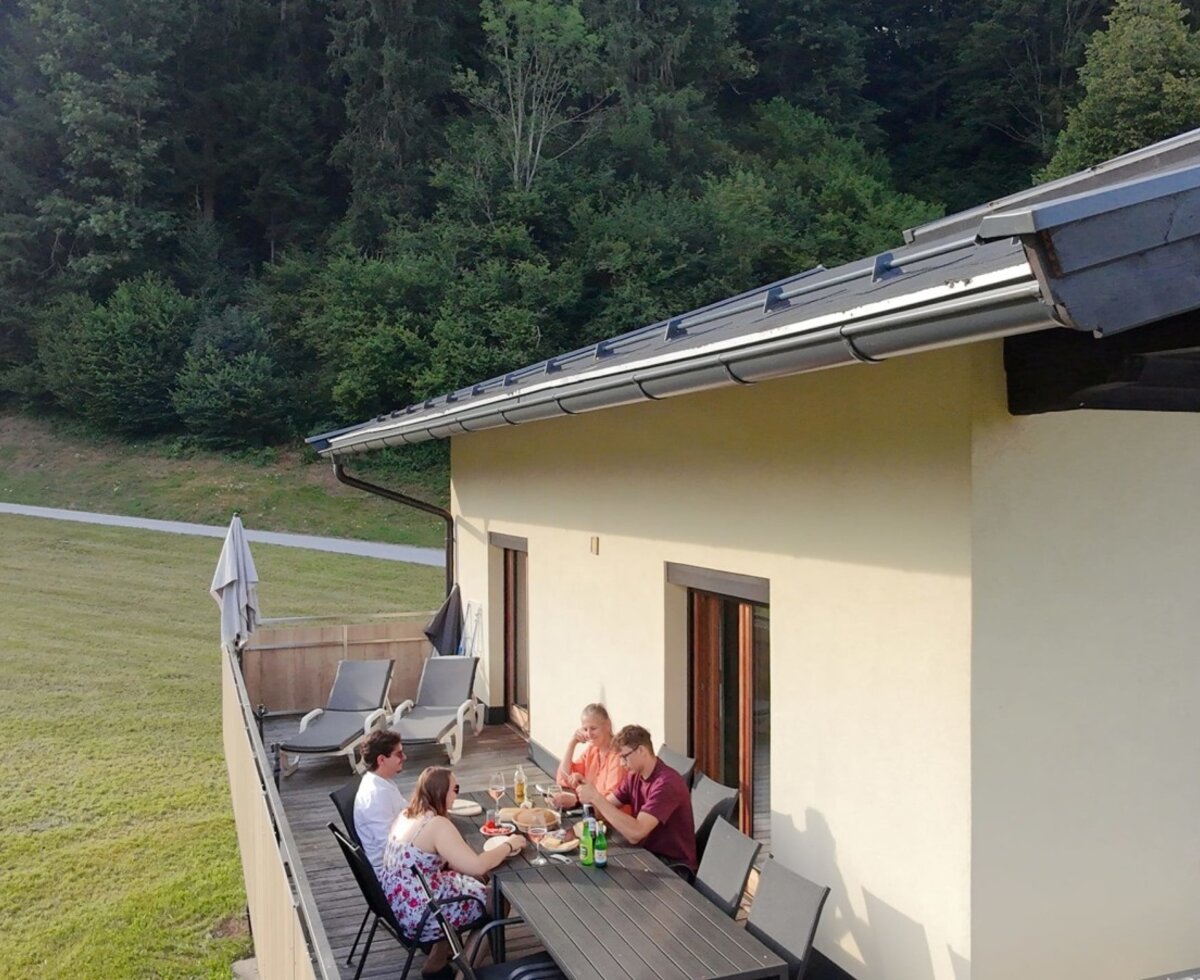 La soleggiata terrazza del agriturismo con un grande tavolo da pranzo e lettini prendisole su uno sfondo idilliaco di boschi.