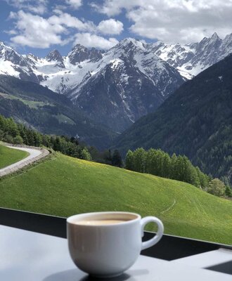 Una tazza di caffè sul balcone dell'agriturismo con un'ampia vista sulle colline verdi e sulle vette innevate.