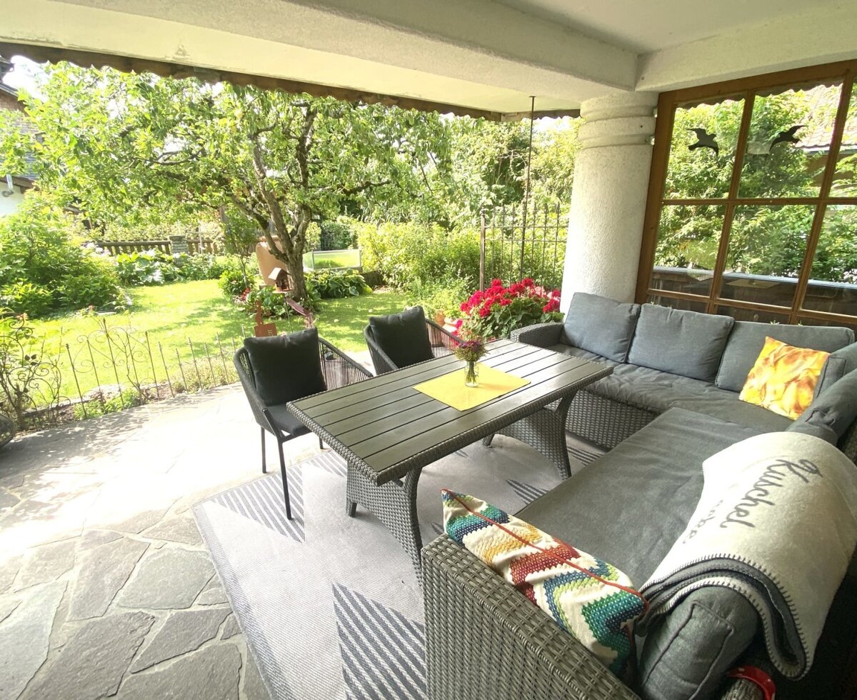 L'invitante terrazza coperta dell'agriturismo, dotata di un'accogliente area salotto, tavolo da pranzo e vista sul rigoglioso giardino.
