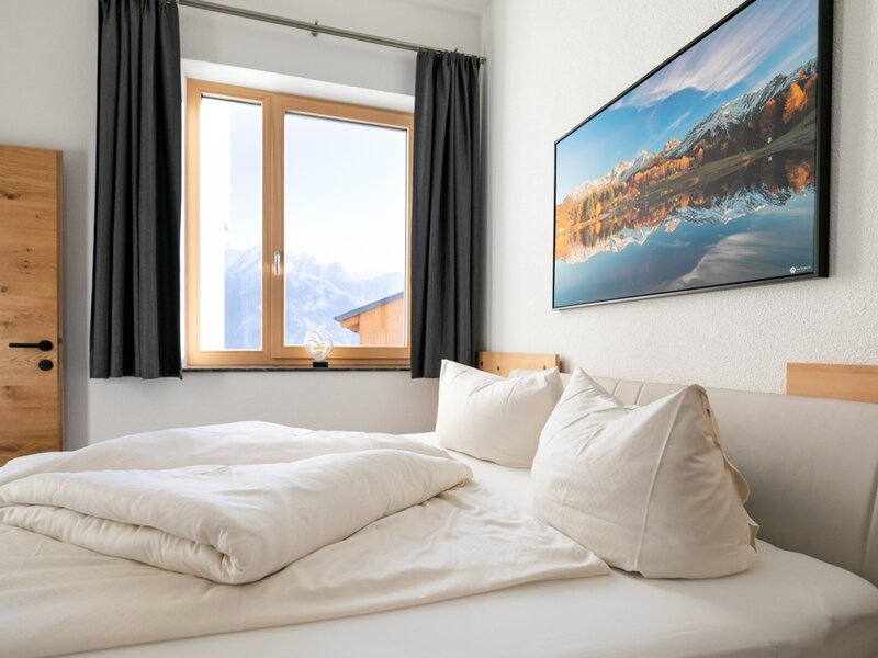 Camera da letto dell'appartamento per vacanze con letto matrimoniale, finestra con vista sulle montagne e porta in legno.