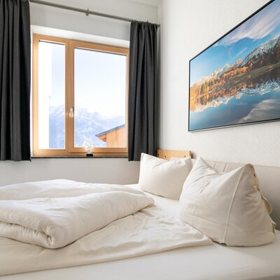 Camera da letto dell'appartamento per vacanze con letto matrimoniale, finestra con vista sulle montagne e porta in legno.