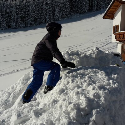 Un bambino gioca in inverno con la neve davanti alla malga.