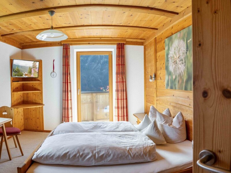 Camera da letto nell'agriturismo con due letti singoli, rivestimento in legno, TV e accesso al balcone.