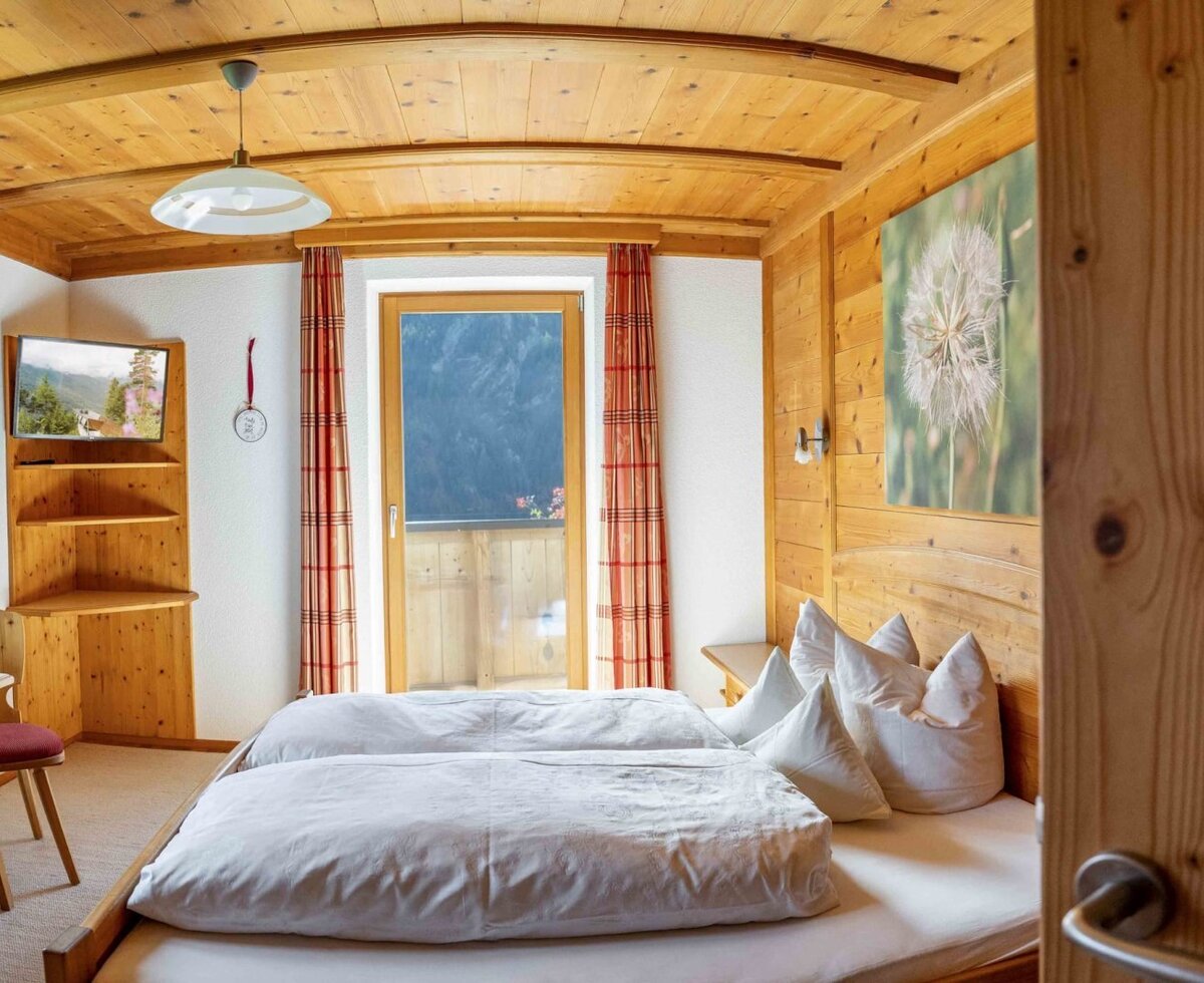 Camera da letto nell'agriturismo con due letti singoli, rivestimento in legno, TV e accesso al balcone.