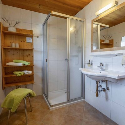 Bagno nell'agriturismo con cabina doccia, lavabo, specchio e scaffale in legno per gli asciugamani.