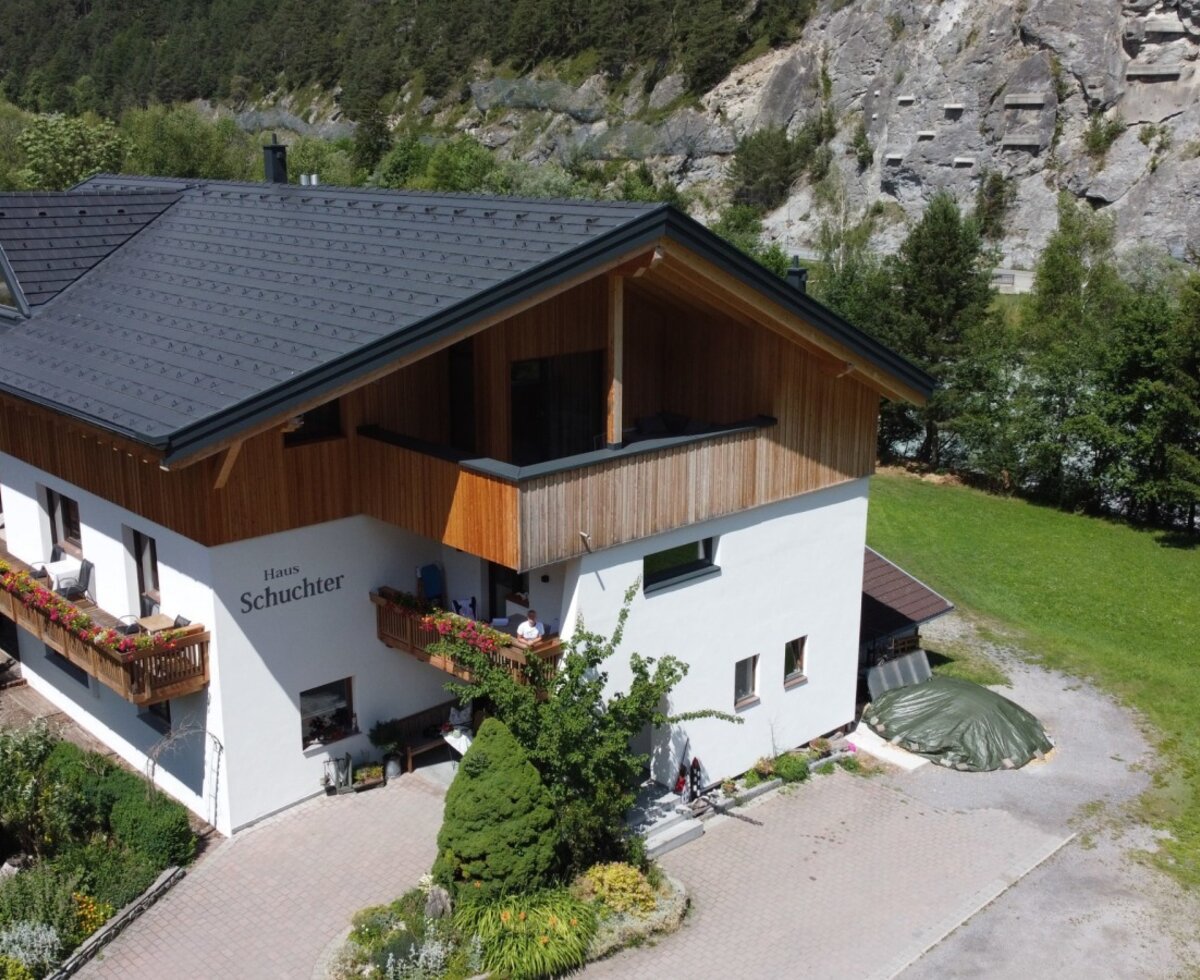Vista esterna del Bauernhof 'Haus Schuchter' con balconi fioriti, circondato da un giardino e un paesaggio montano.
