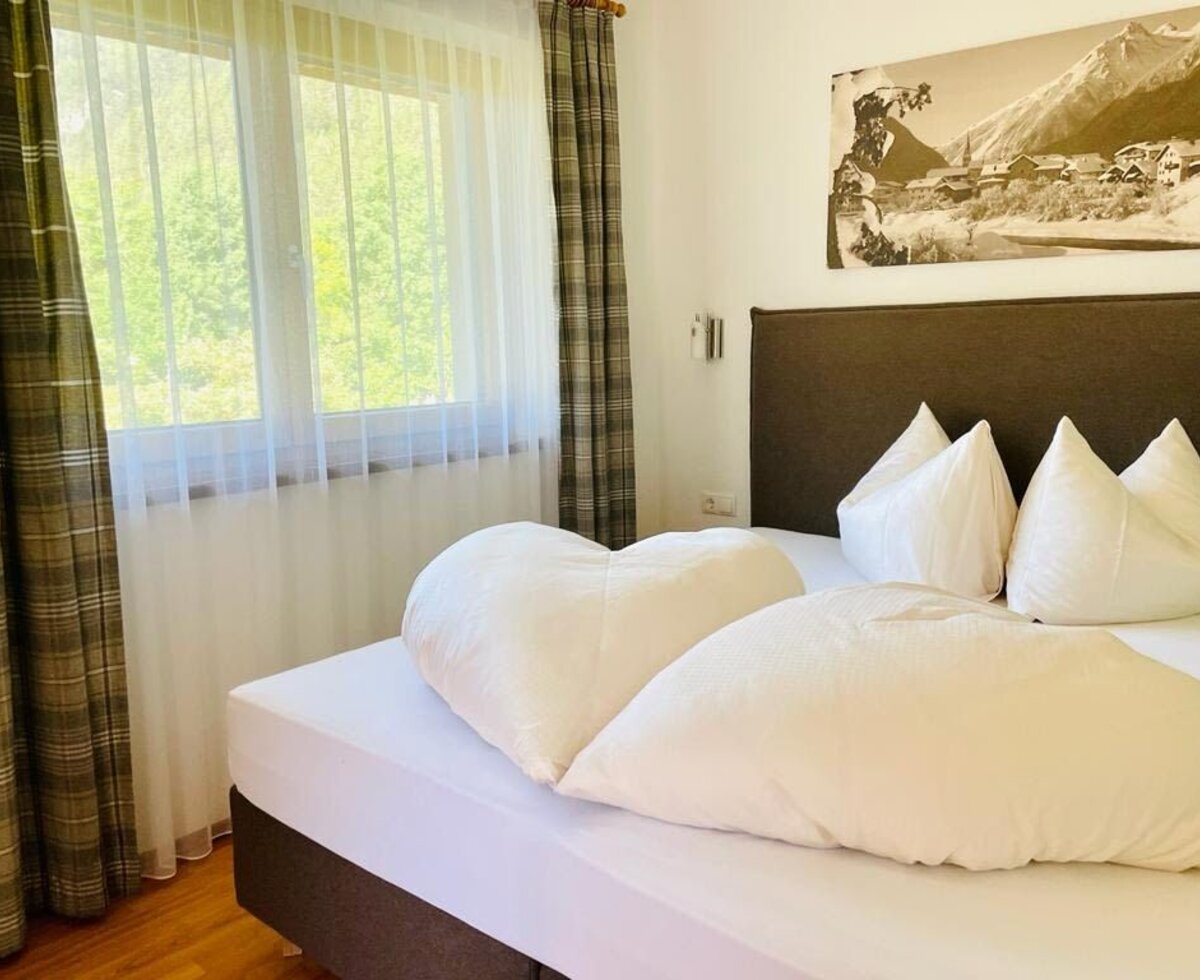 Letto matrimoniale nella camera del Bauernhof con vista sul verde dalla finestra e un quadro a parete con motivo alpino.