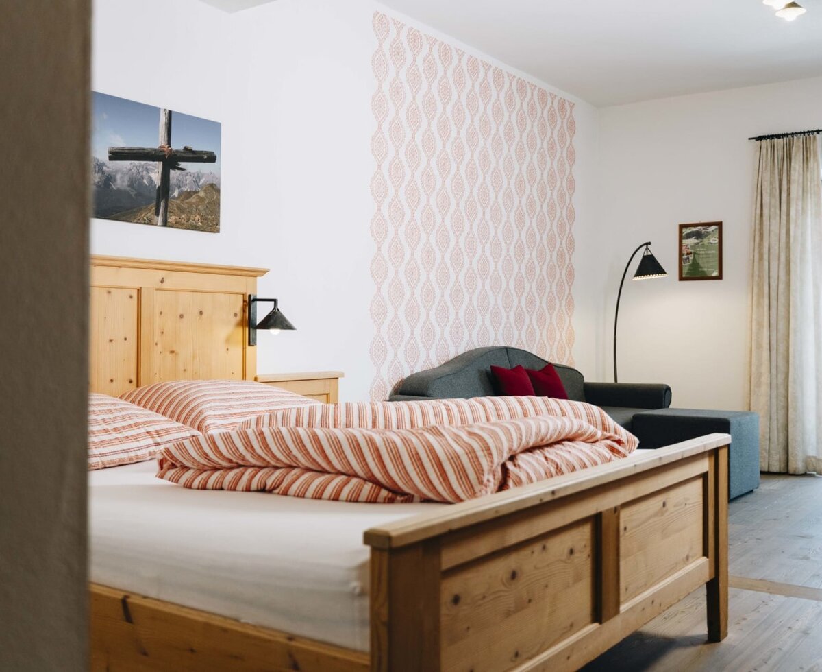 Camera da letto nel Bauernhof con letto in legno, divano e accesso al balcone.