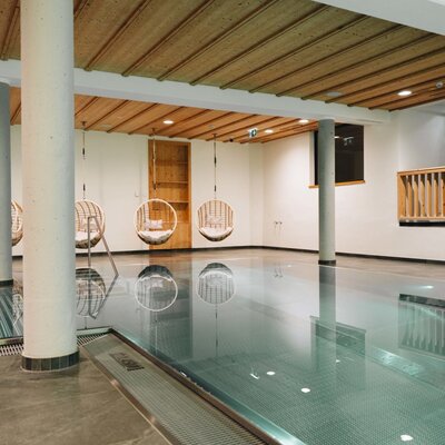 La piscina interna dell'agriturismo con diverse sedie sospese a bordo piscina e un soffitto in legno.