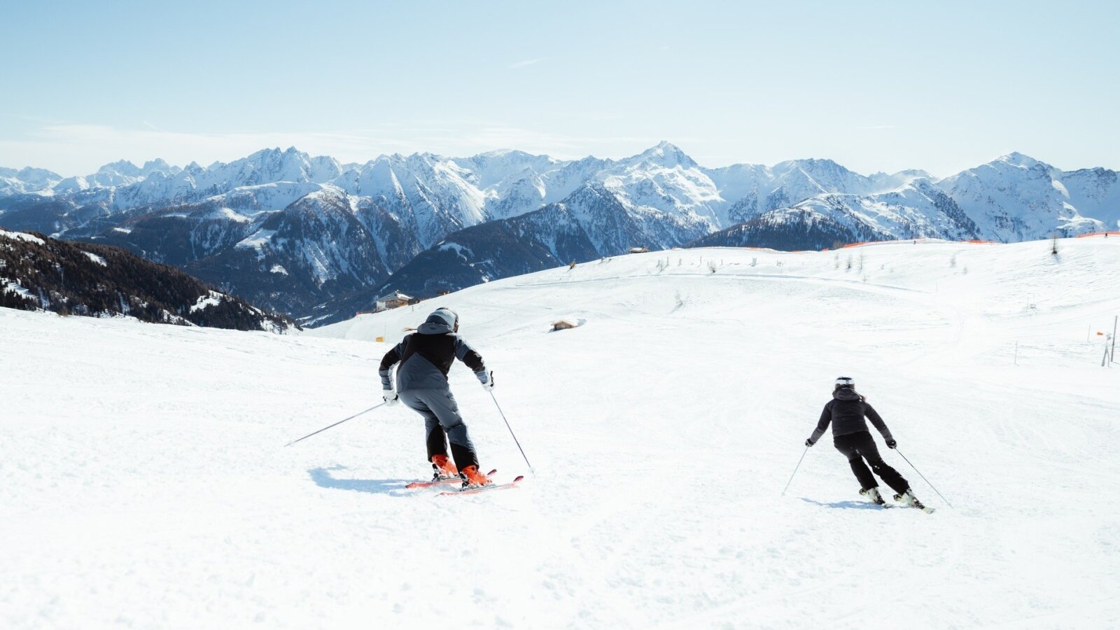 Due persone che sciano su una pista innevata con un panorama montano.