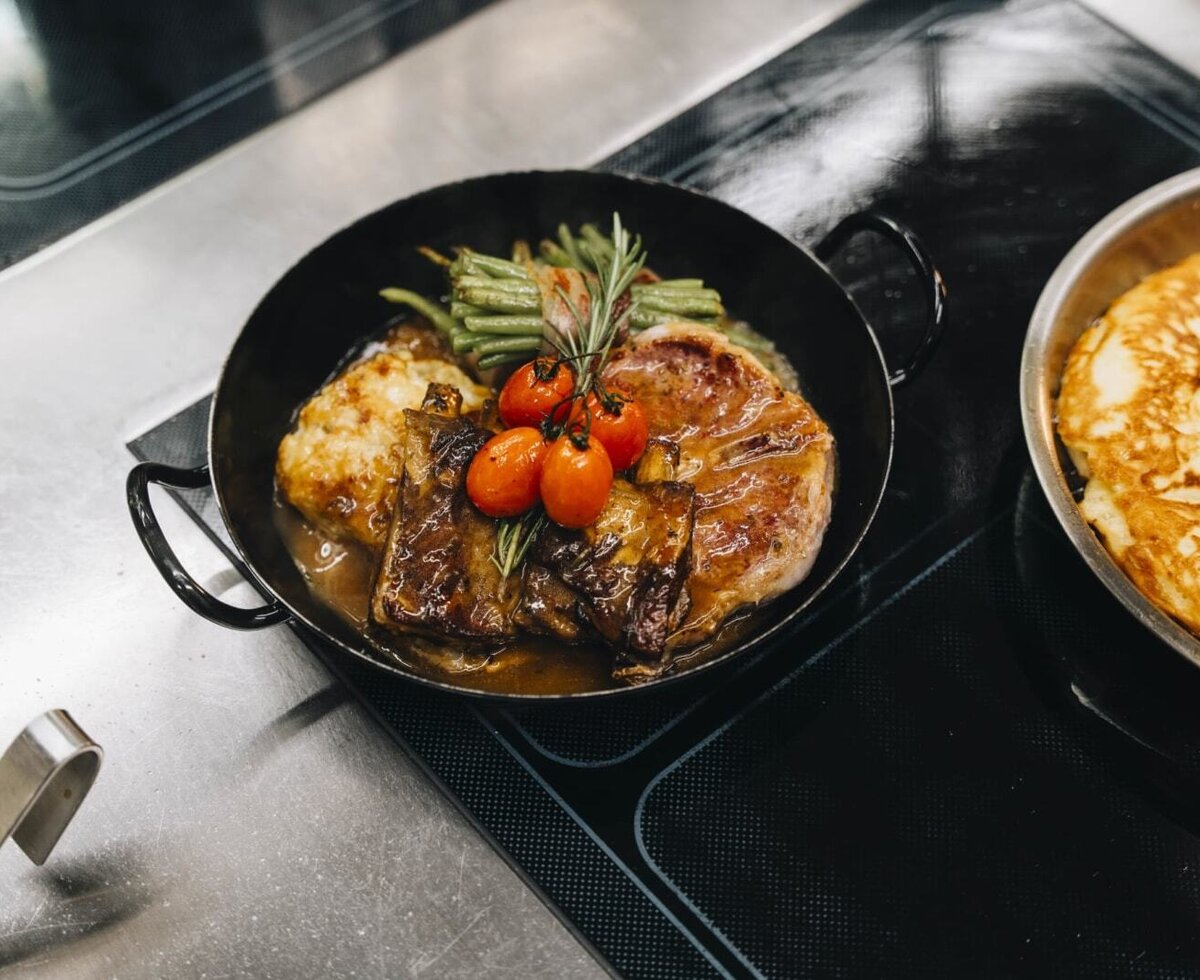 Piatto di carne sostanzioso con costolette, contorno di patate, fagiolini e pomodorini, servito in padella nell'agriturismo.