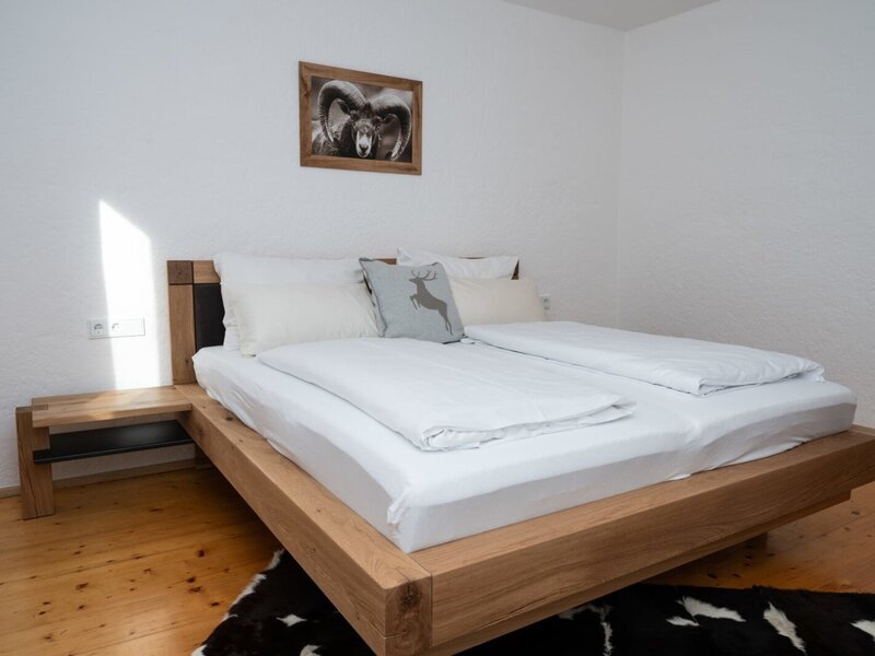 Camera da letto nell'appartamento con un letto matrimoniale in legno, comodino integrato e pavimento in legno.