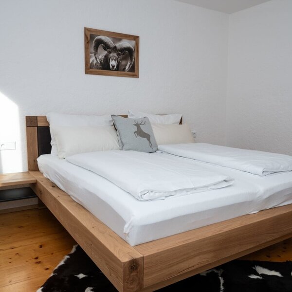 Camera da letto nell'appartamento con un letto matrimoniale in legno, comodino integrato e pavimento in legno.