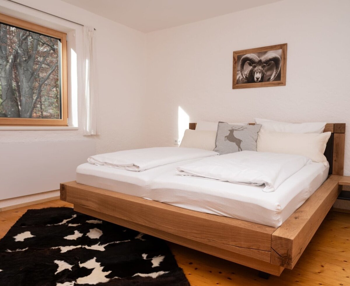 Camera da letto nell'appartamento con letto matrimoniale, pavimento in legno, un tappeto bianco e nero e una finestra con vista sugli alberi.