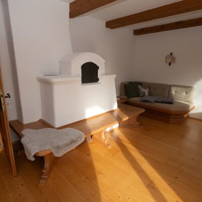 Zona giorno dell'Appartamento con stufa in maiolica tradizionale, panca in legno, divano e travi in legno a vista.