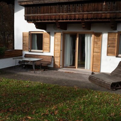 La terrazza privata dell'Apartment offre un tavolo da pranzo esterno, una panca, una sedia a sdraio in legno e accesso diretto a un'area verde.