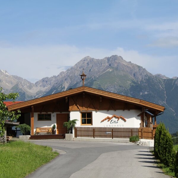 L'esterno degli Ap­par­te­ments, caratterizzato da uno stile rustico tradizionale, con sfondo montano e vialetto d'accesso.