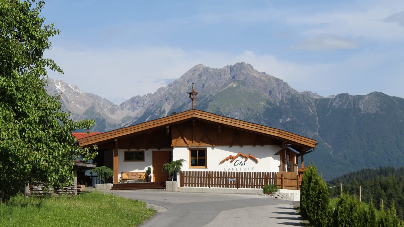 L'esterno degli Ap­par­te­ments, caratterizzato da uno stile rustico tradizionale, con sfondo montano e vialetto d'accesso.