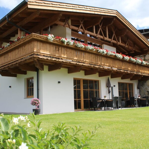 Vista esterna degli Ap­par­te­ments con balconi in legno fioriti, un prato verde e un'area salotto esterna.