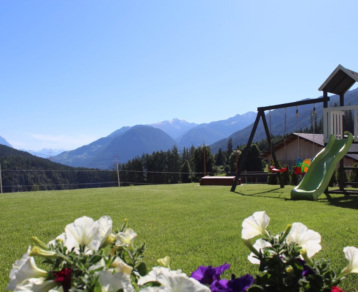 Prato verde con parco giochi per bambini e vista sulle montagne, parte degli Ap­par­te­ments.