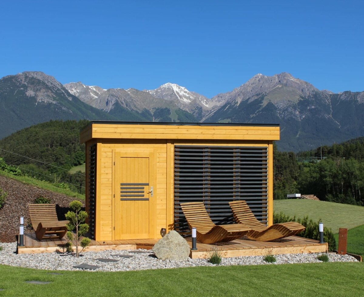 Sauna esterna degli Ap­par­te­ments con terrazza in legno, sedie a sdraio e vista sulle montagne.