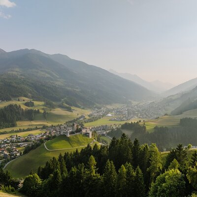 Vista sulla valle con un paese e un castello, circondata da montagne e foreste.