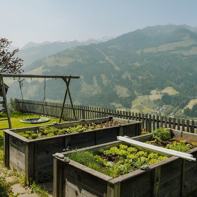 Aiuole rialzate con piante fresche e un parco giochi per bambini nell'agriturismo con vista sulle montagne.