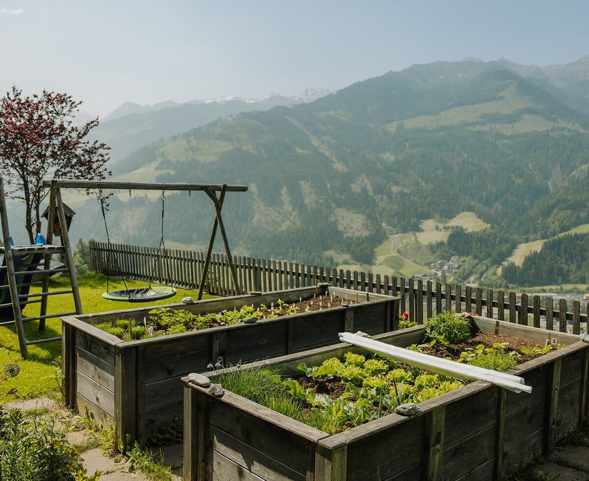 Aiuole rialzate con piante fresche e un parco giochi per bambini nell'agriturismo con vista sulle montagne.