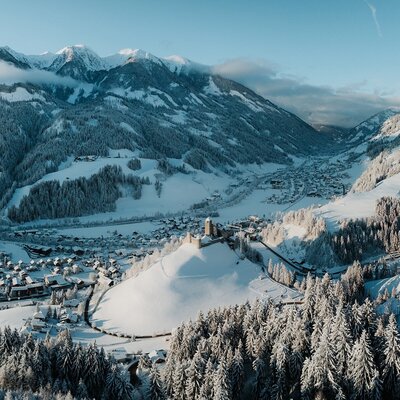 Vista sulla valle innevata con un villaggio e un castello, circondata da montagne innevate.