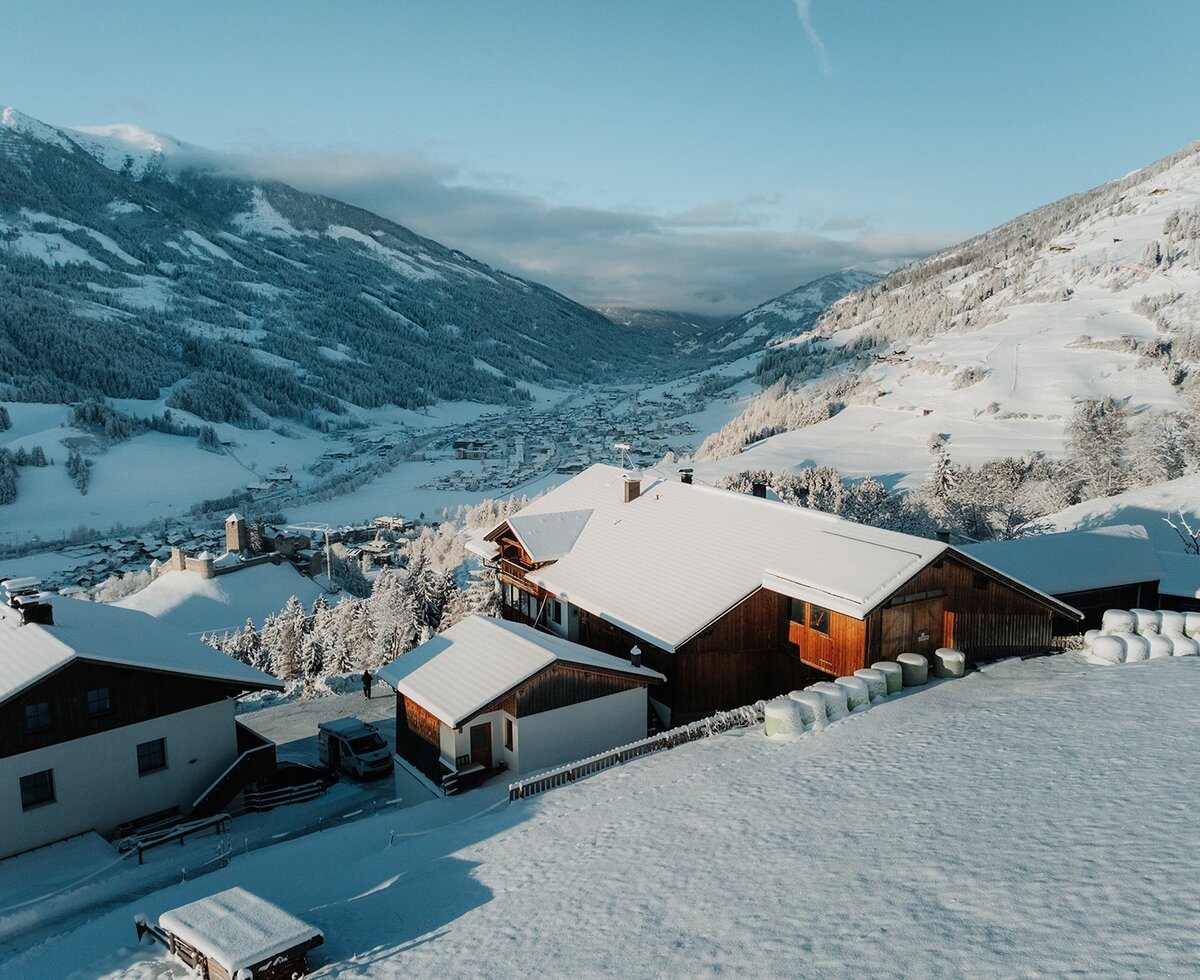 Il maso in inverno, circondato da neve e montagne, con vista sulla valle.