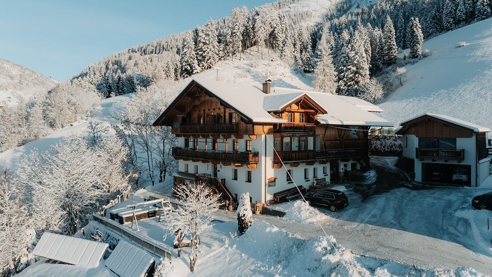 Il maso in inverno con balconi e un parco giochi per bambini sulla terrazza, circondato da montagne innevate.
