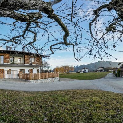 Vista esterna del maso 'Zuahaus' con facciata bianca, rivestimento in legno e il paesaggio montano circostante.