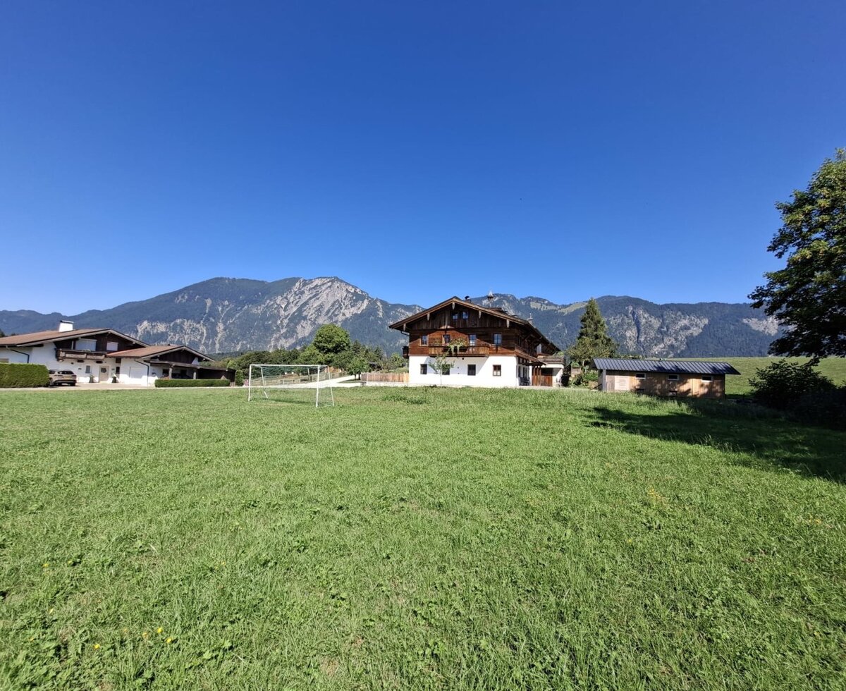L'accogliente agriturismo circondato da un ampio prato verde con una porta da calcio e una suggestiva vista sulle montagne sullo sfondo.
