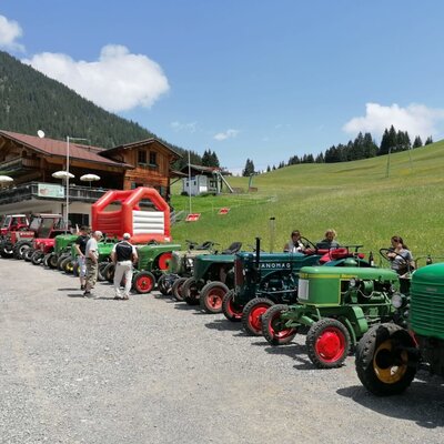 Una fila di trattori d'epoca parcheggiati davanti all'accogliente agriturismo, circondato da verdi prati alpini e da un castello gonfiabile.