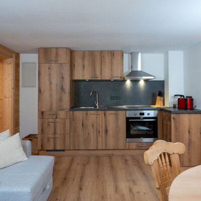 Cucina moderna negli Ap­par­te­ments con mobili in legno, lavello, piano cottura e forno, aperta sulla zona giorno.